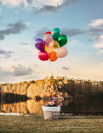 baby in a basket lifted by colorful balloons beside a lake portrait photography