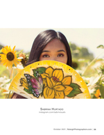 woman peeking over a hand-painted fan in a sunflower field portrait photography
